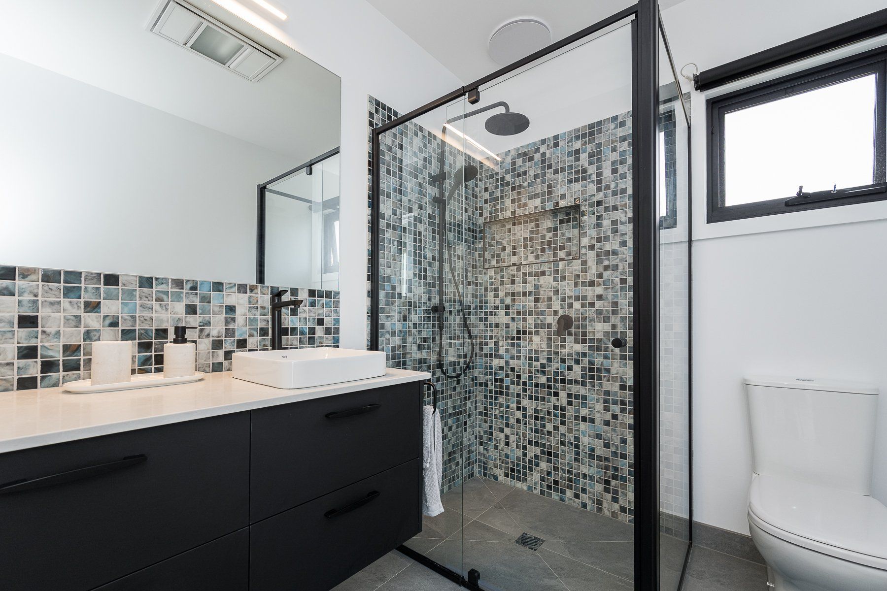 A bathroom with a walk in shower , sink , toilet and mirror.
