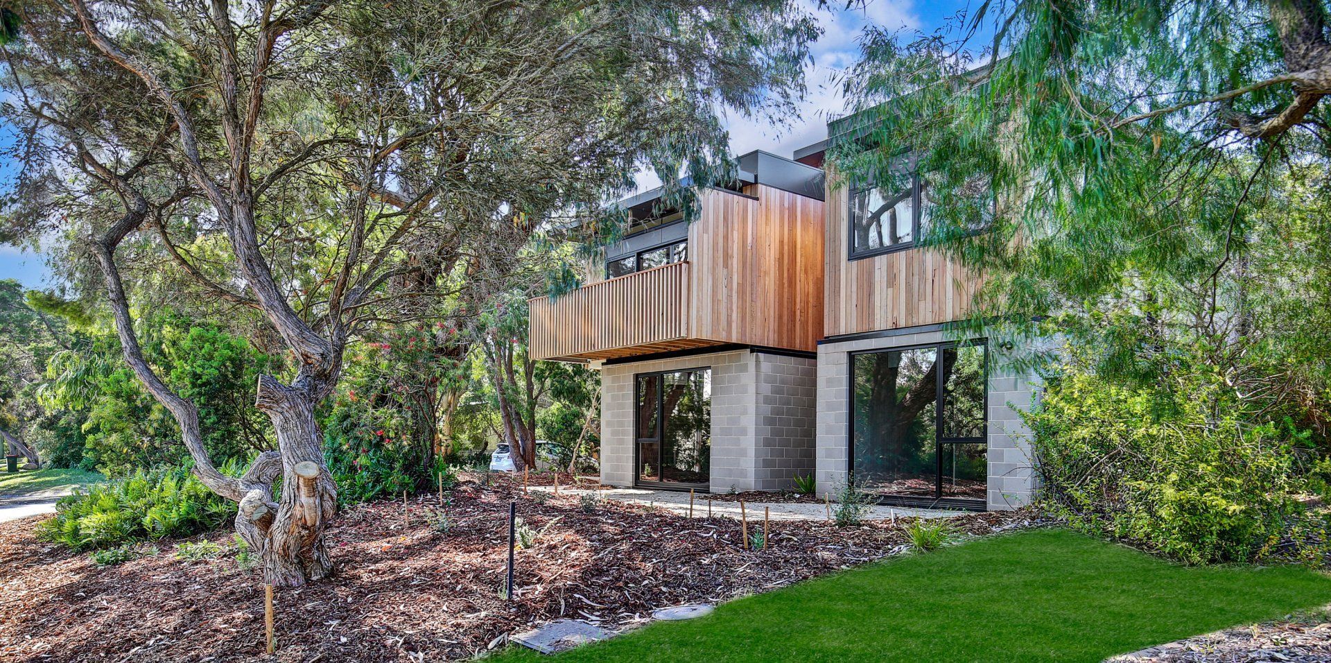 Modern house with wood and concrete exterior, surrounded by trees and green grass.