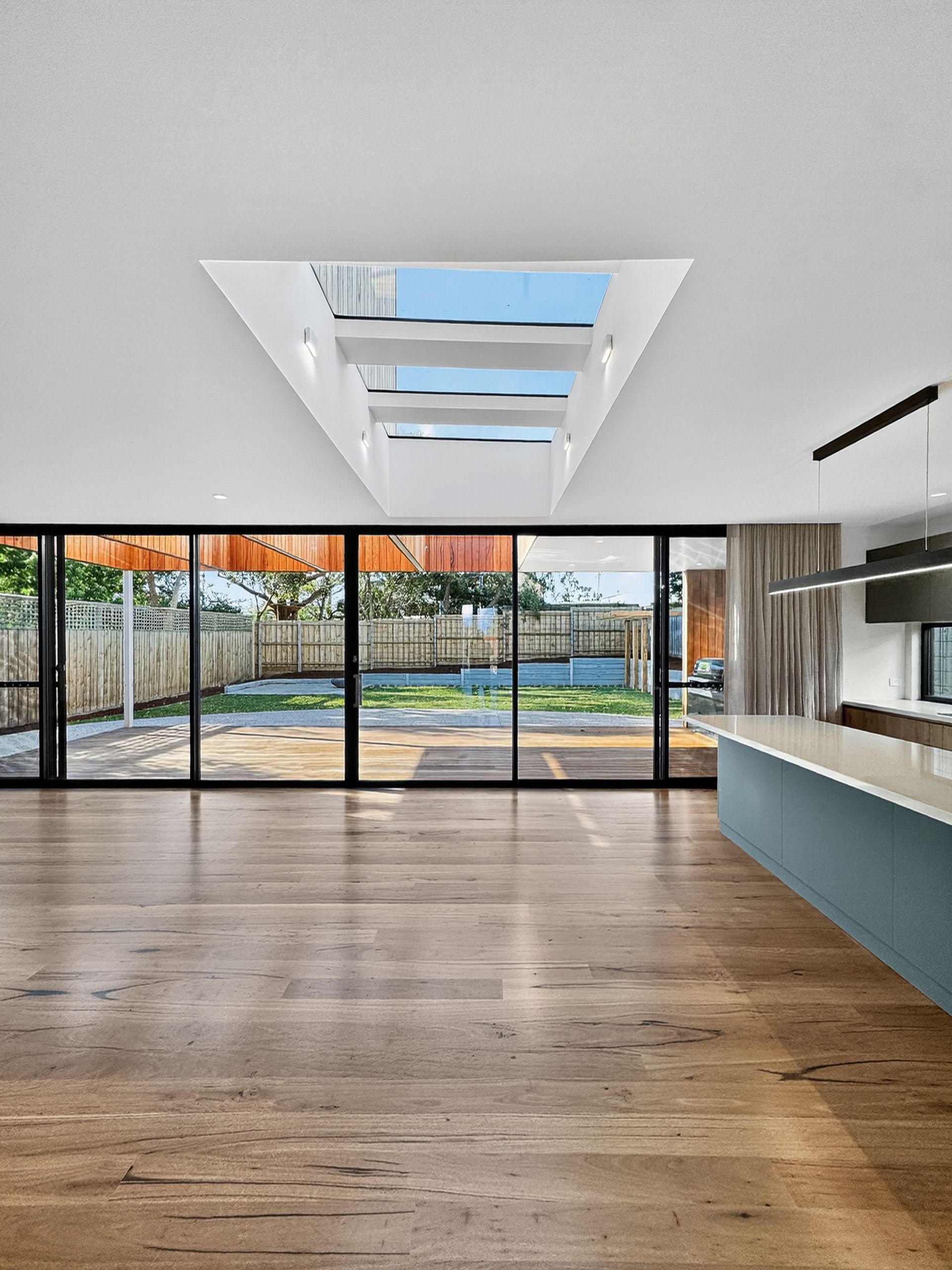 Interior view of a modern home with large glass doors leading to a backyard. A triangular skylight is overhead.