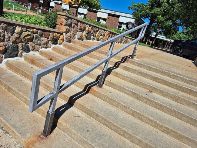 Outdoor concrete stairs with a silver handrail beside a stone wall and parked car.
