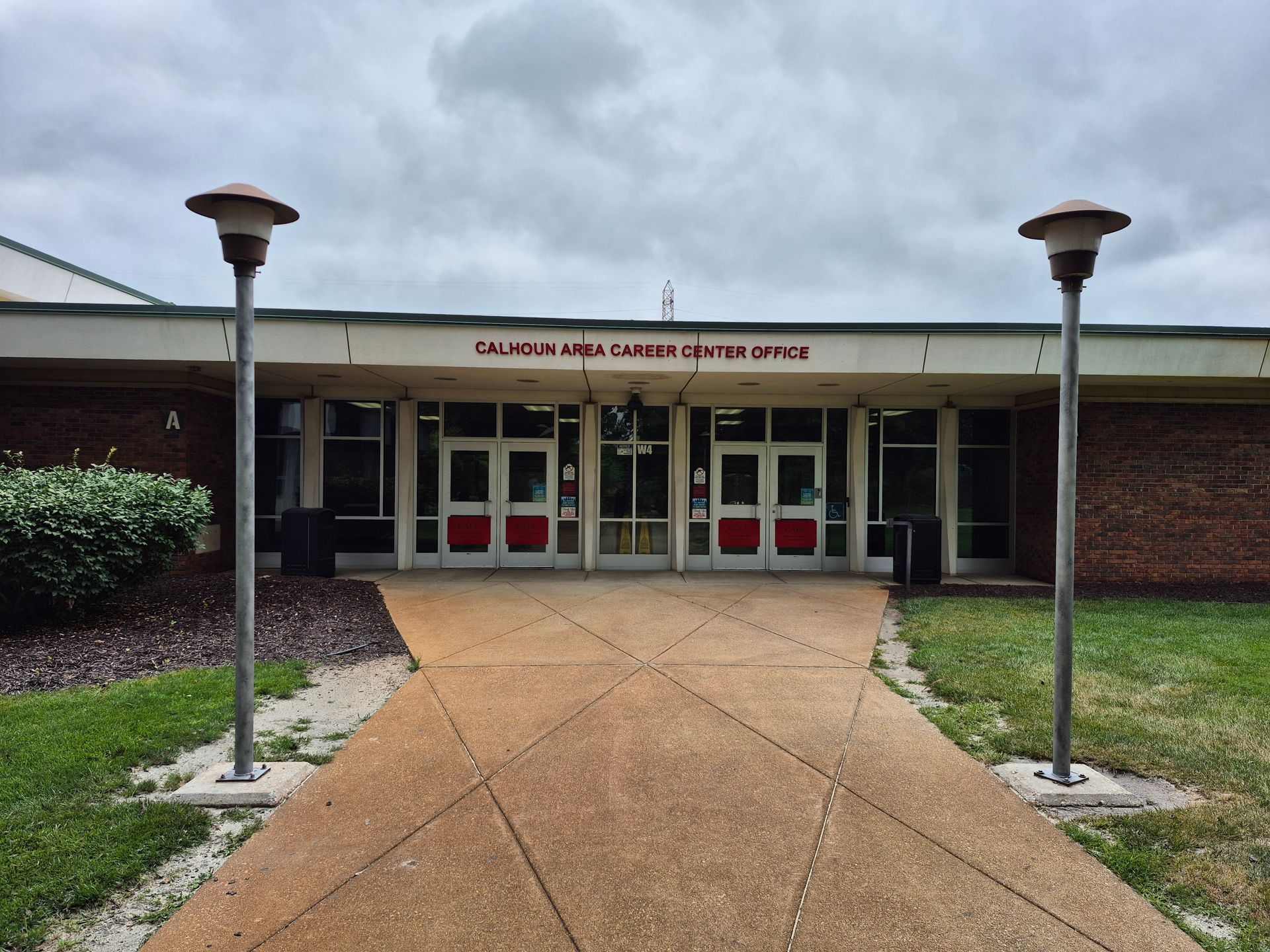 Front entrance of a public building with red double doors, tan walkway, and two lamp posts.