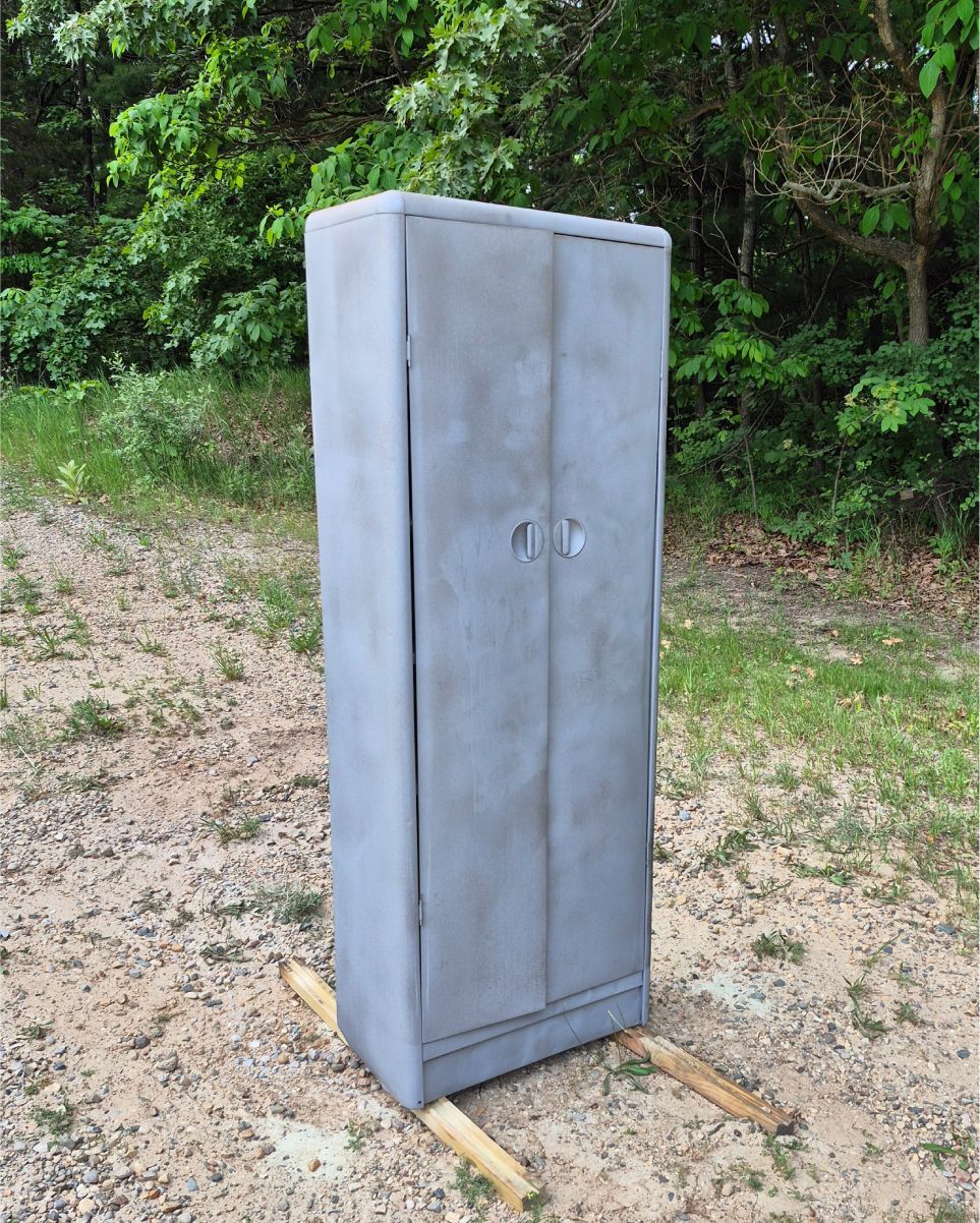 Gray metal storage cabinet outdoors on grass near trees