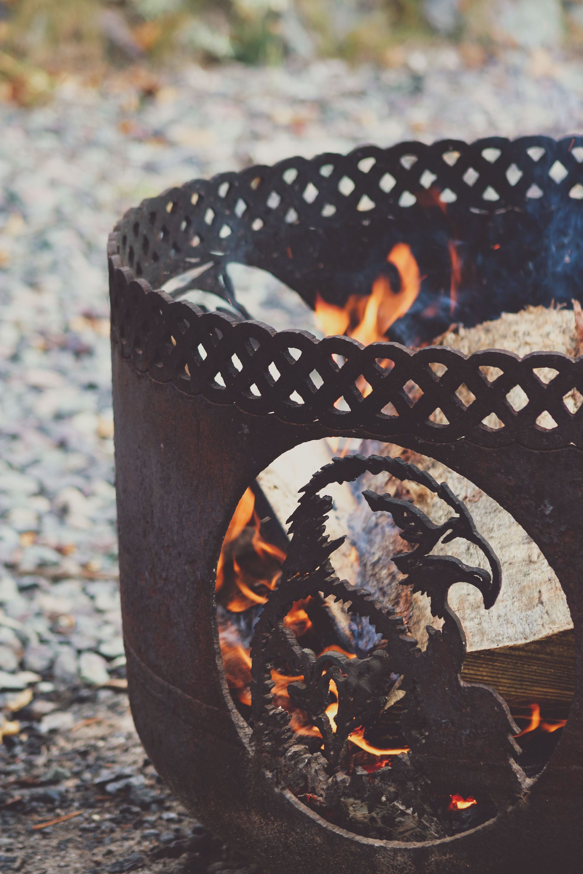 Black metal fire pit with orange flames burning on a stone surface outdoors
