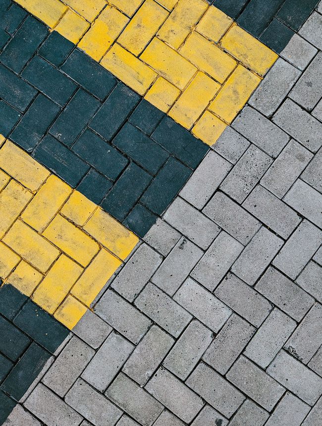 Diagonal rows of yellow, dark teal, and gray brick paving stones