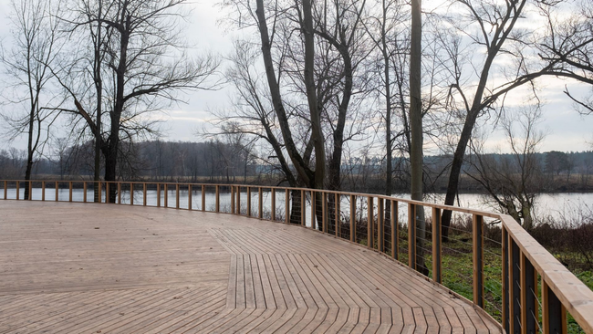 Curved wooden boardwalk beside a river with bare trees in winter