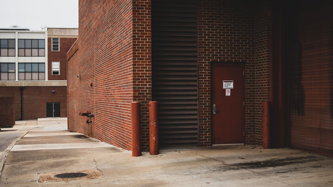 Brick building entrance with red door, stairwell, and concrete walkway