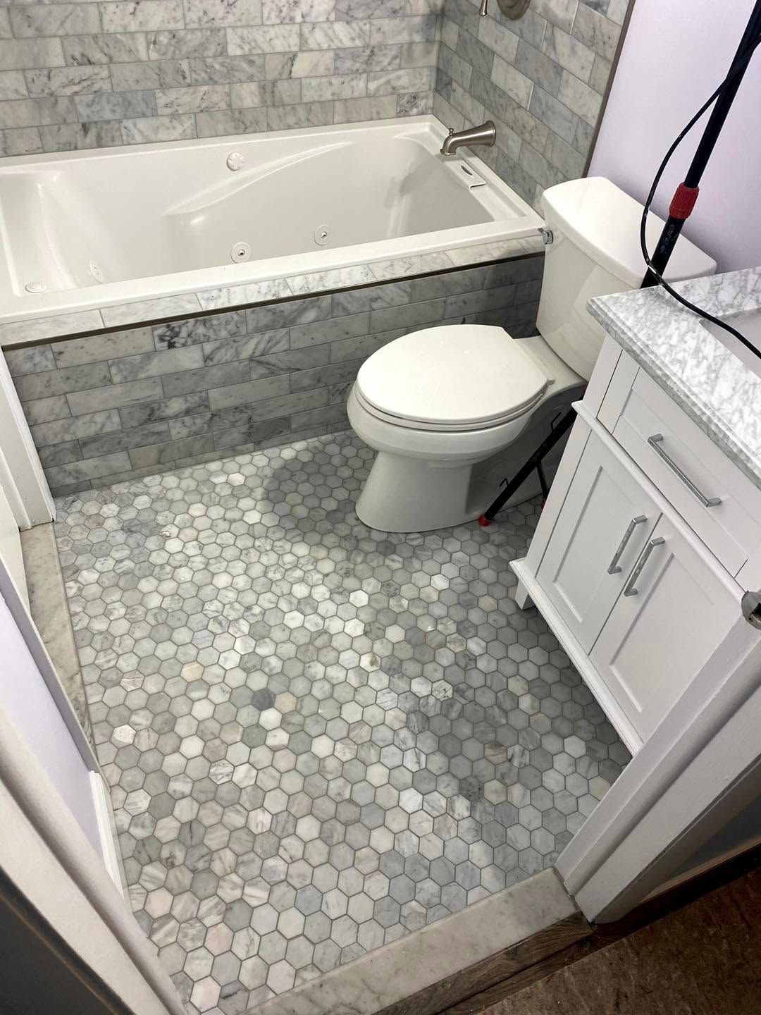 Small bathroom with a tiled bathtub, toilet, and gray hexagon floor tiles