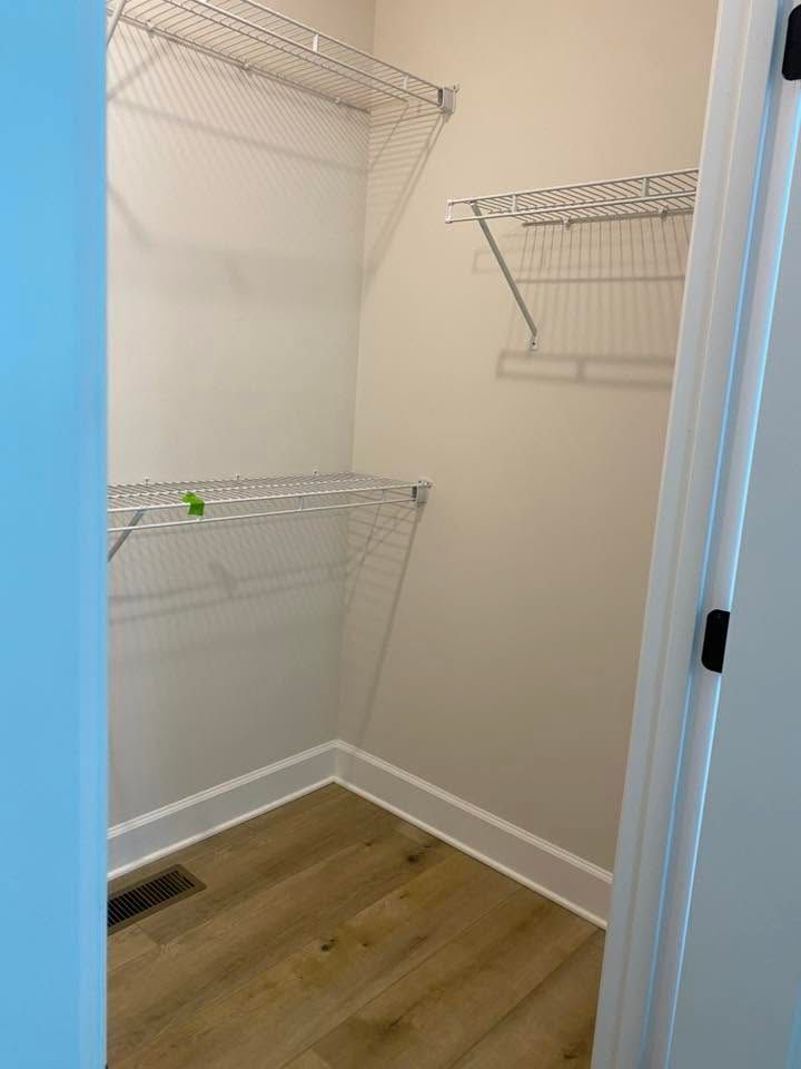 Small empty closet with white wire shelves, beige walls, and wood flooring.