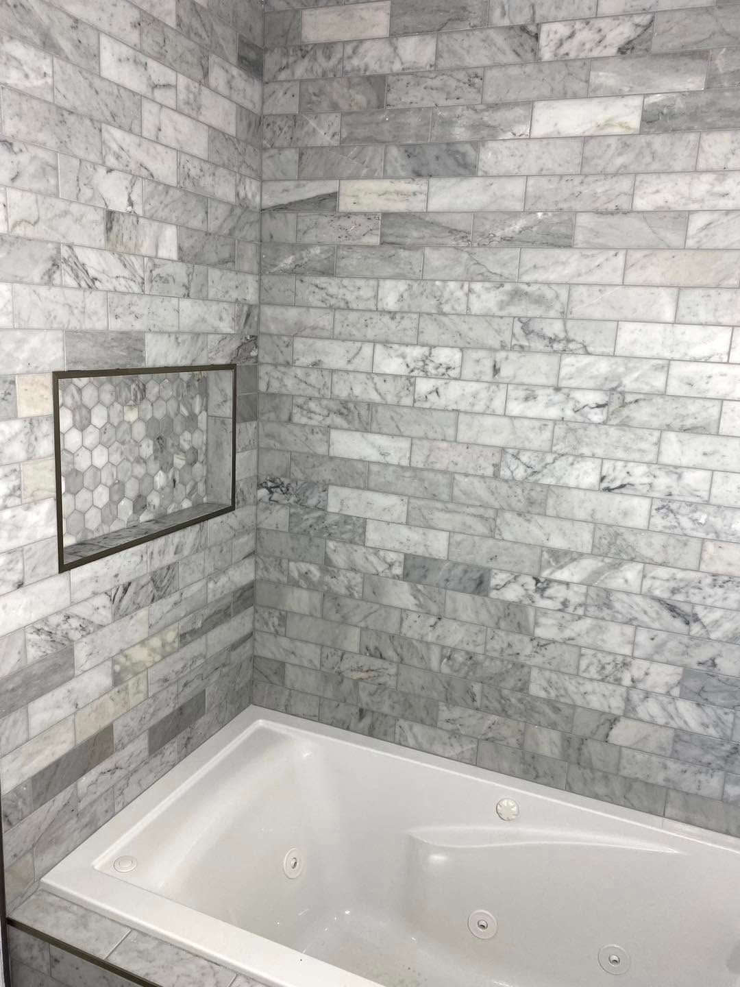 White corner bathtub in a gray stone-tiled bathroom alcove