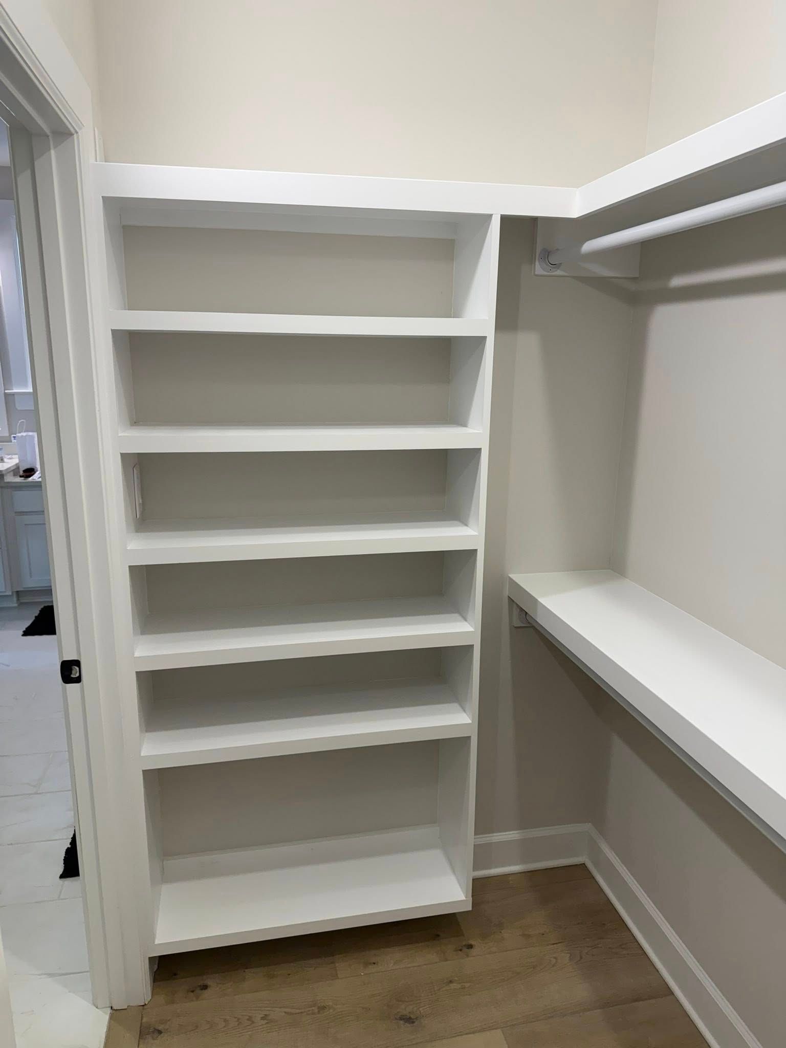 Empty walk-in closet with white built-in shelving and hanging rods on wood flooring.