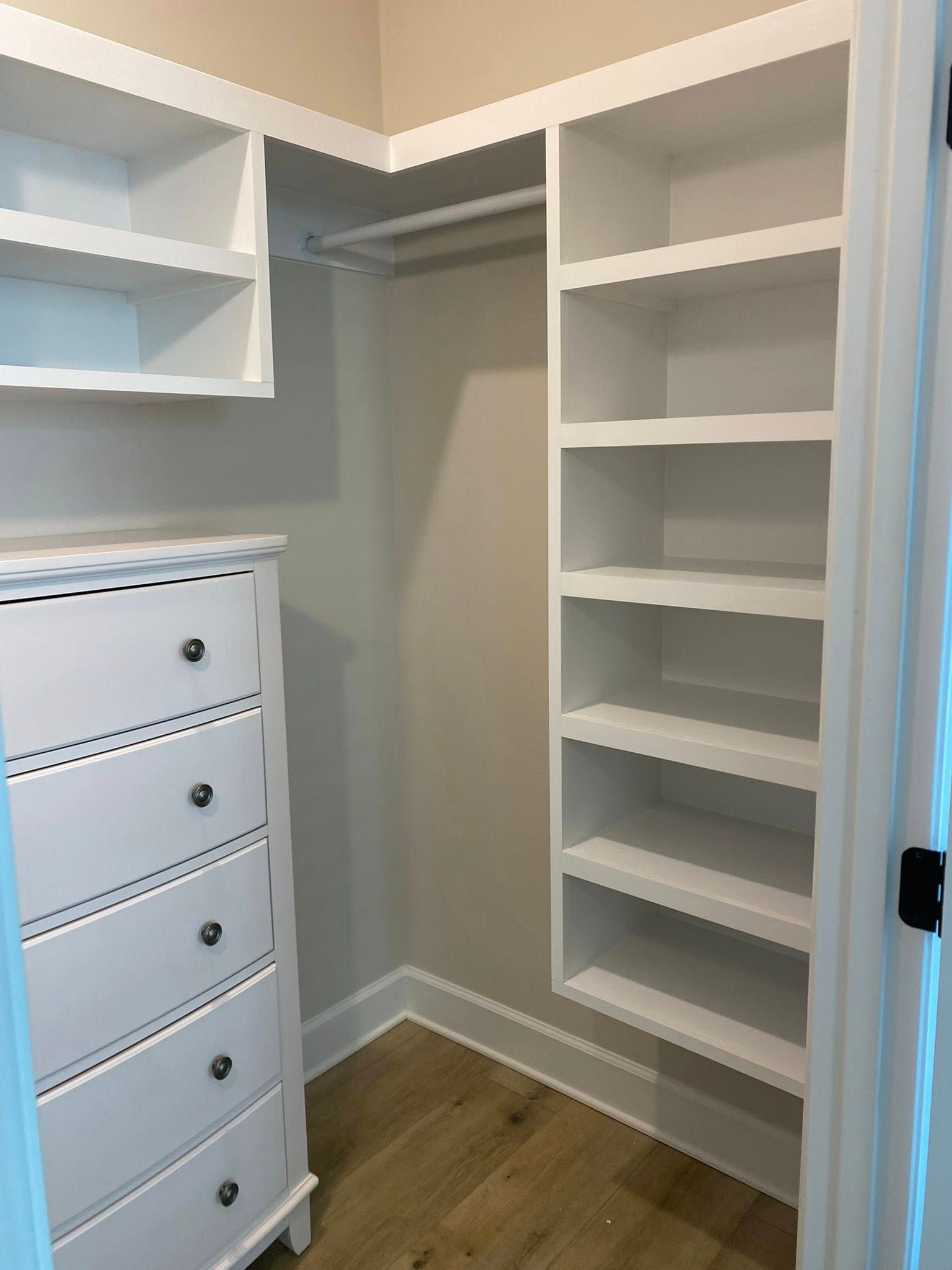 Empty white walk-in closet with built-in shelves, drawers, and wood flooring