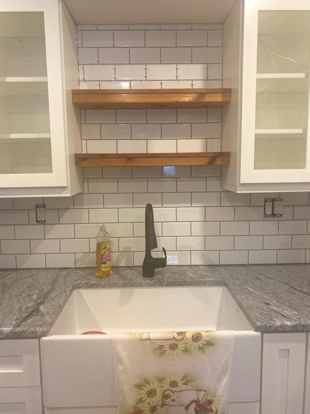 White kitchen sink with gray countertop, subway tile backsplash, open shelves, and a floral dish towel draped over the front.