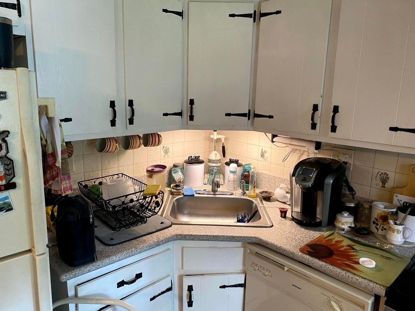 Small white kitchen with cabinets, sink, countertop items, coffee maker, and dish rack.