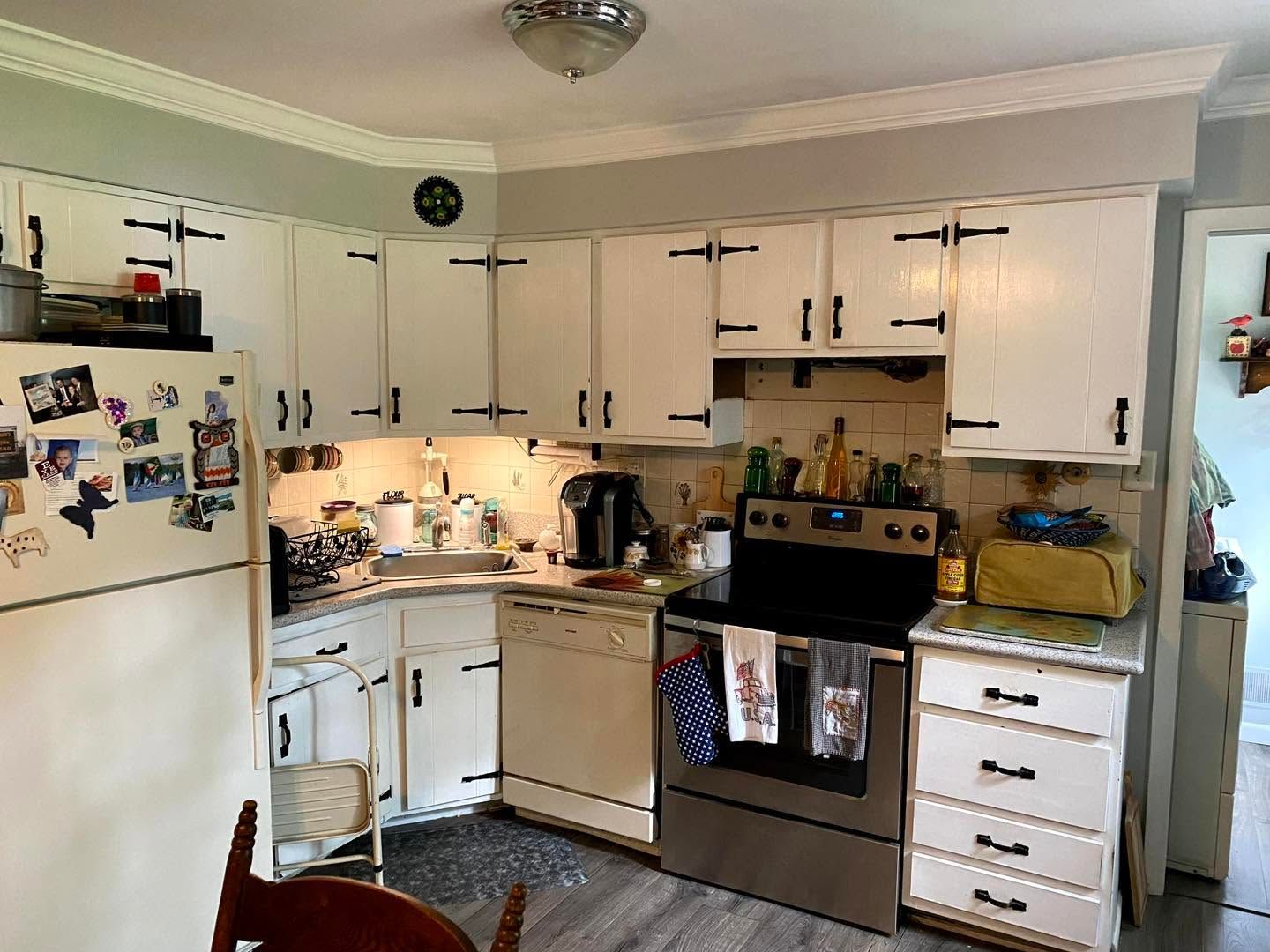 White kitchen with cabinets, refrigerator covered in magnets, and stainless stove and dishwasher under warm ceiling light