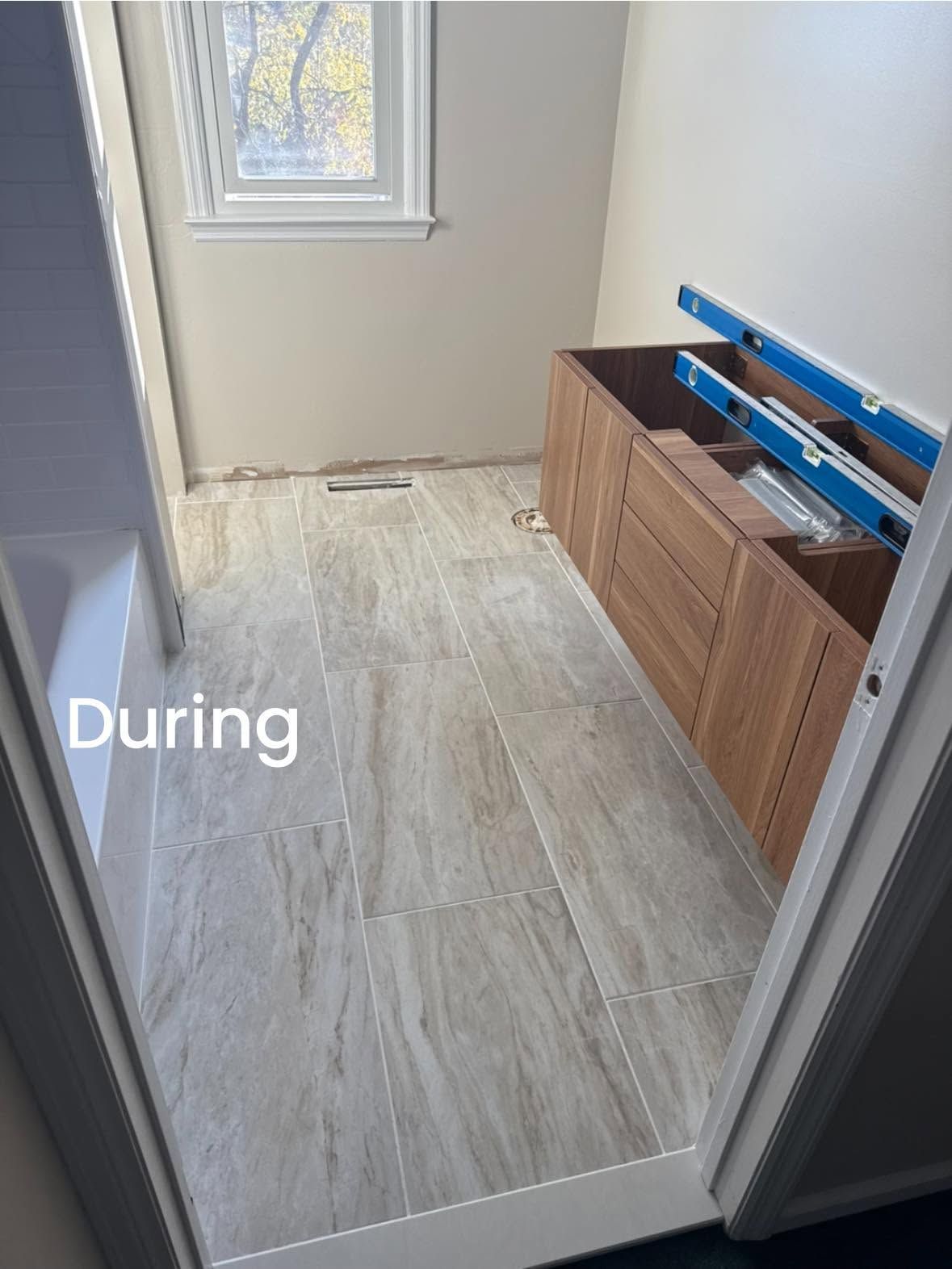 Narrow hallway during renovation with new wood-look flooring, window light, and cabinet materials on the right