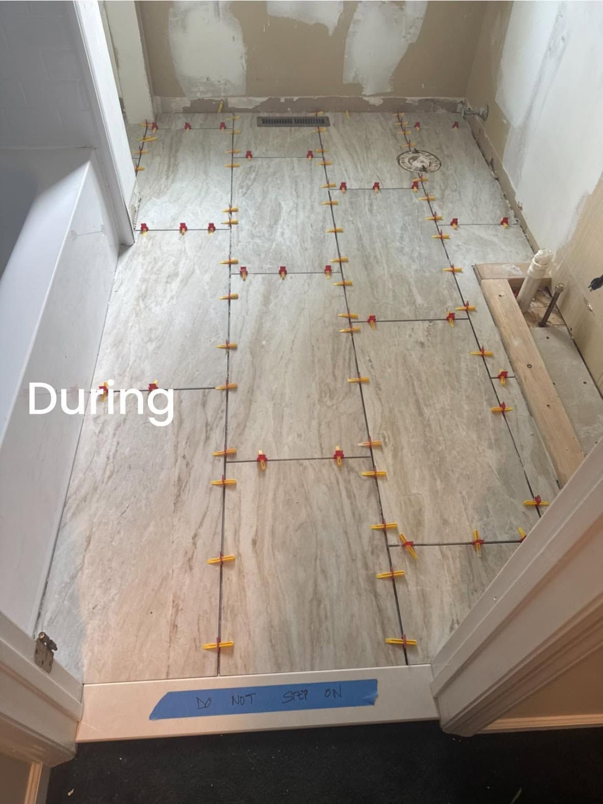 Tiled bathroom floor under repair, with leveling clips and spacers laid across the tiles.