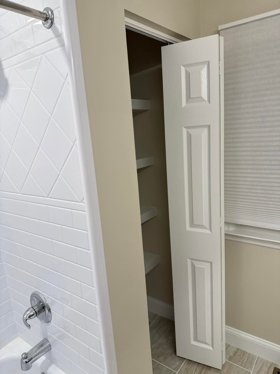 Bathroom with shower, white tiled wall, and open closet door revealing shelves.