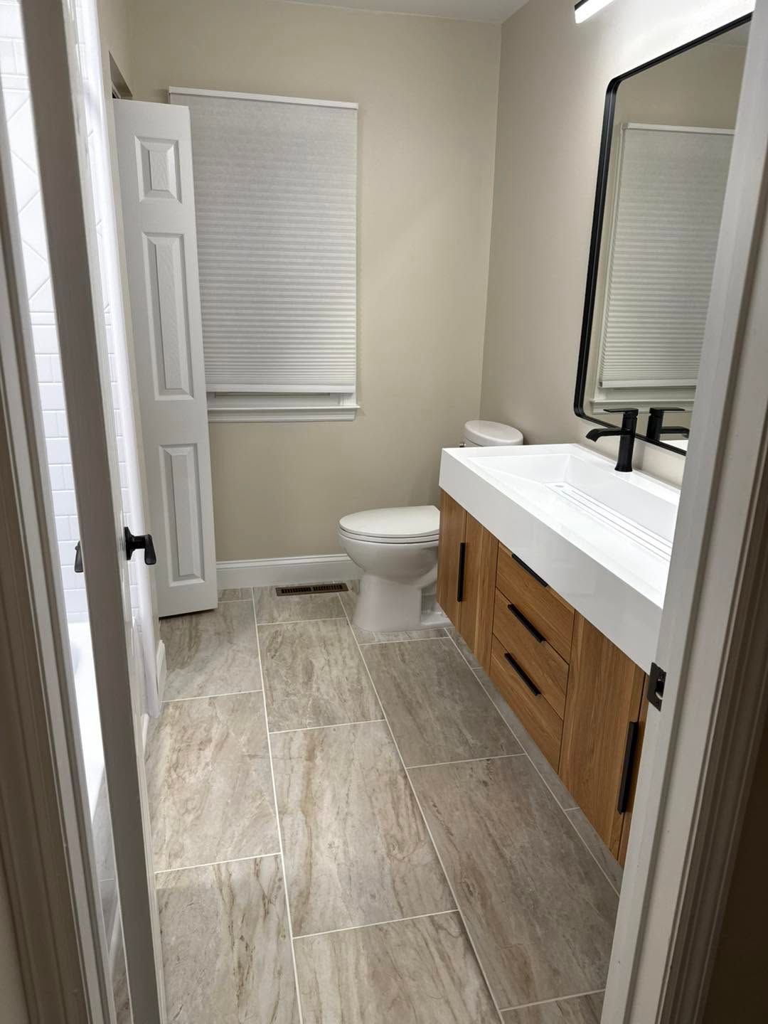 Bathroom with vanity, mirror, toilet, and window blinds in neutral tones.