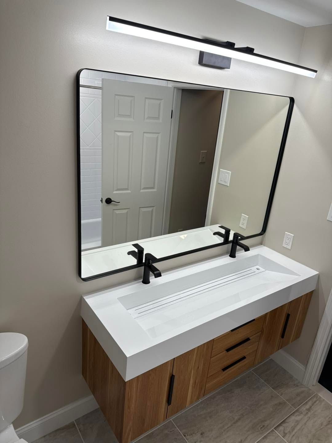 Accessible bathroom vanity with large mirror, dual faucets, and wood cabinet under bright lighting