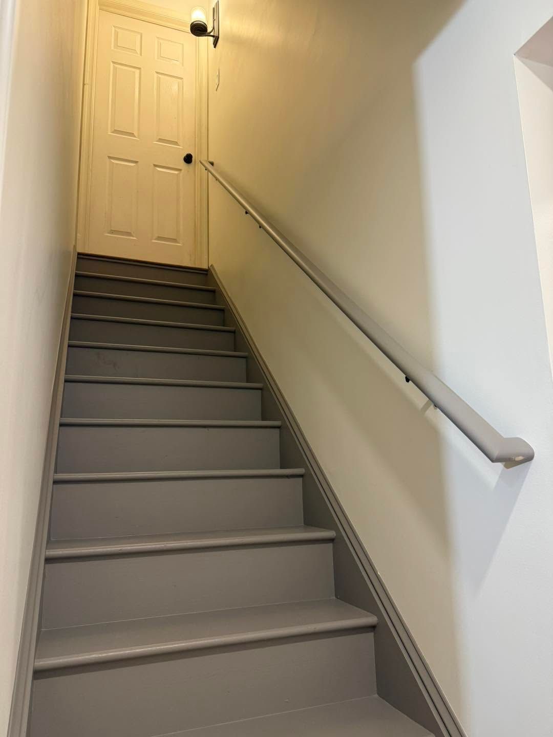 Narrow indoor staircase with gray steps, white walls, and a closed door at the top