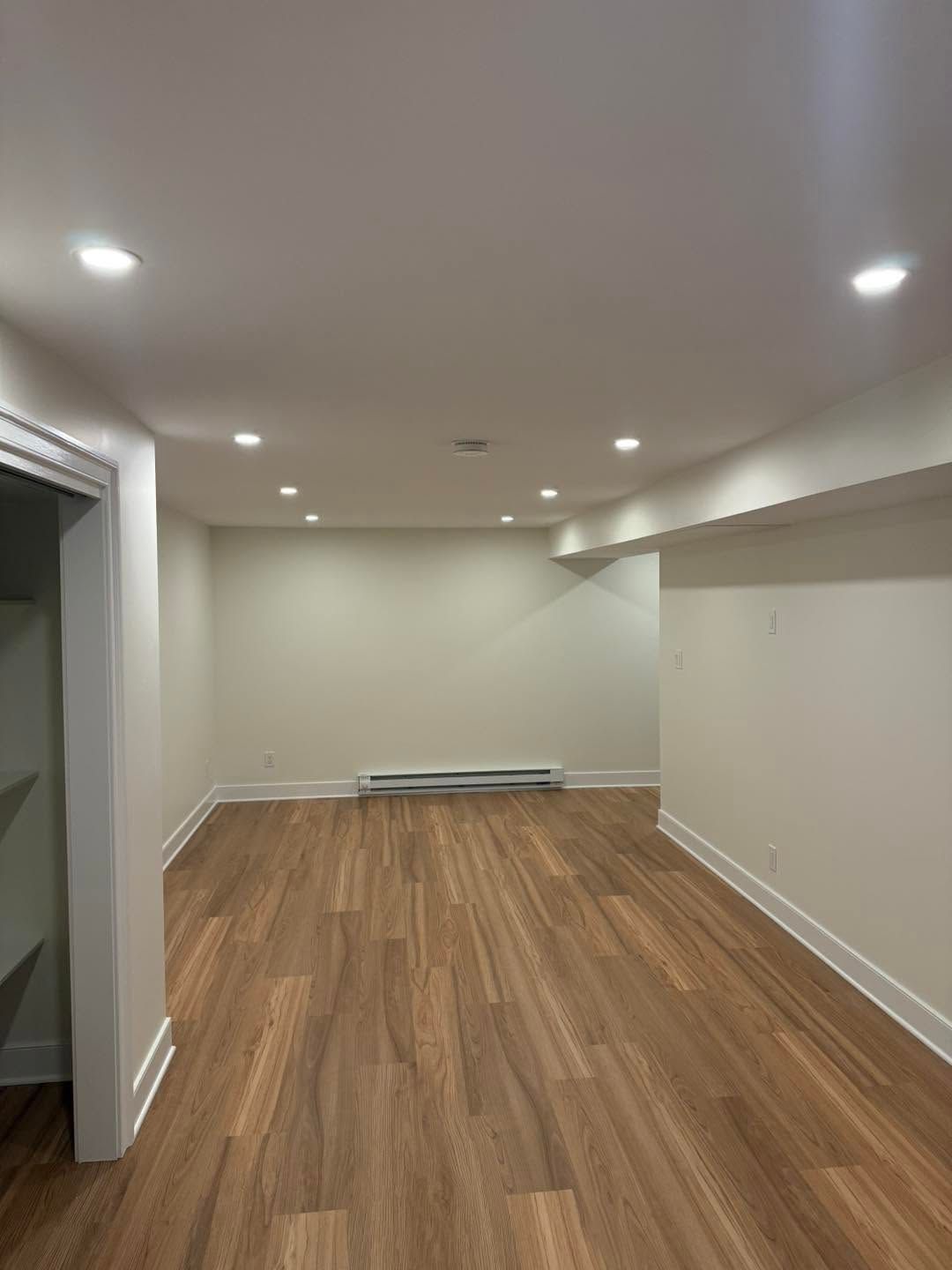 Empty finished basement room with wood floors, recessed lights, and white walls