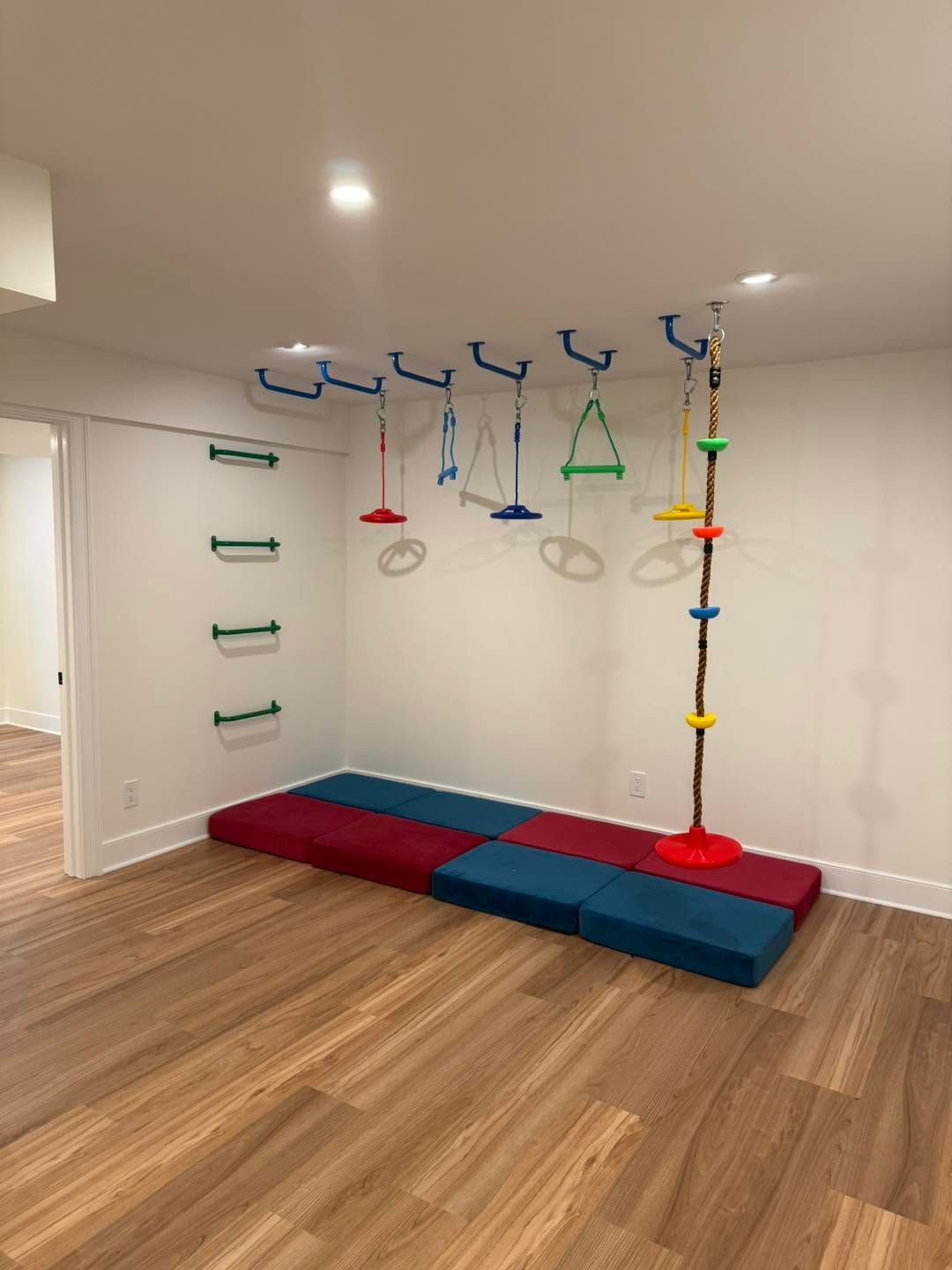 Indoor sensory play room with hanging gym equipment, wall ladder, and foam mats on a wooden floor