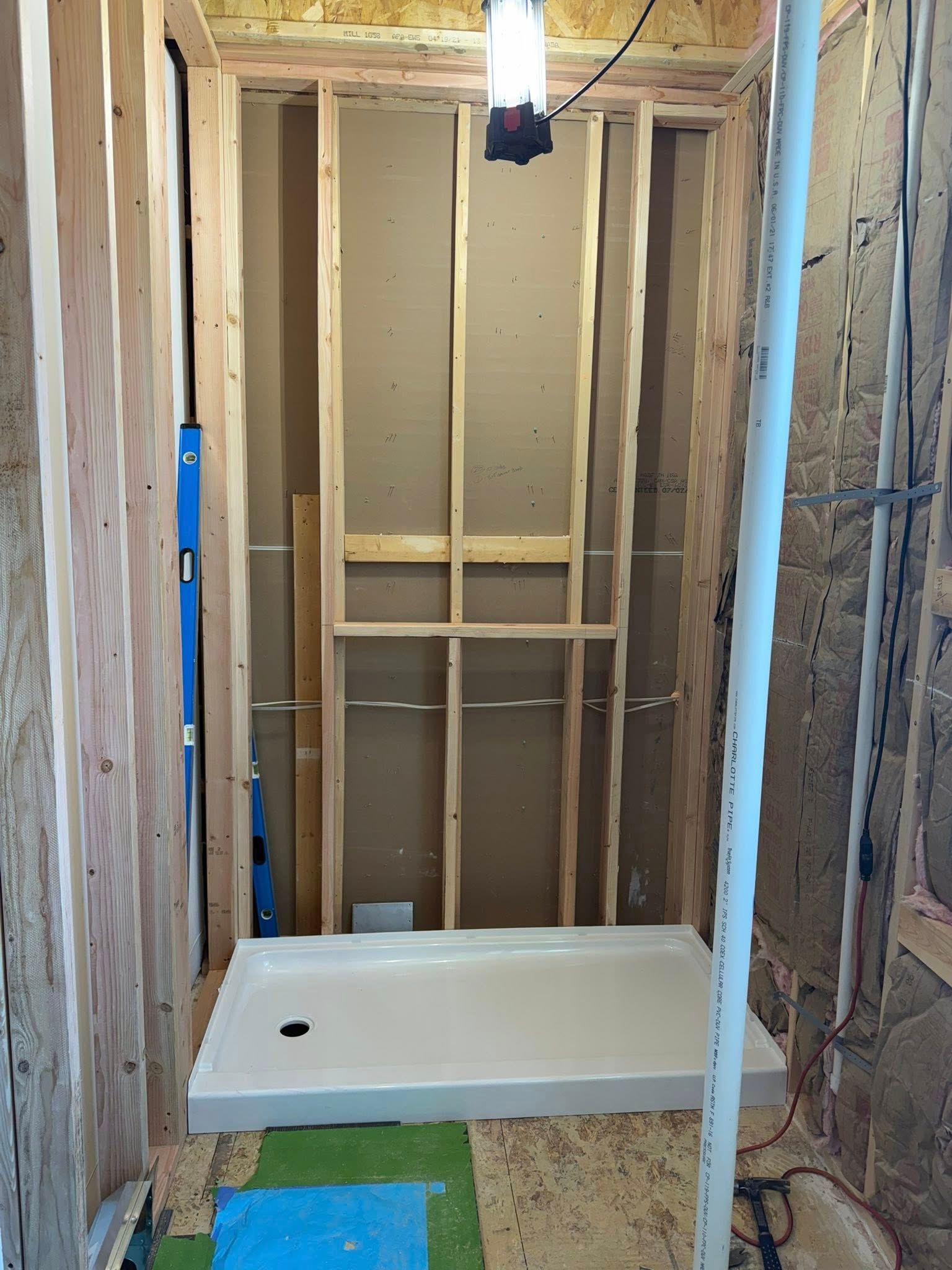 Unfinished bathroom with a shower pan, exposed framing, and a hanging light fixture.