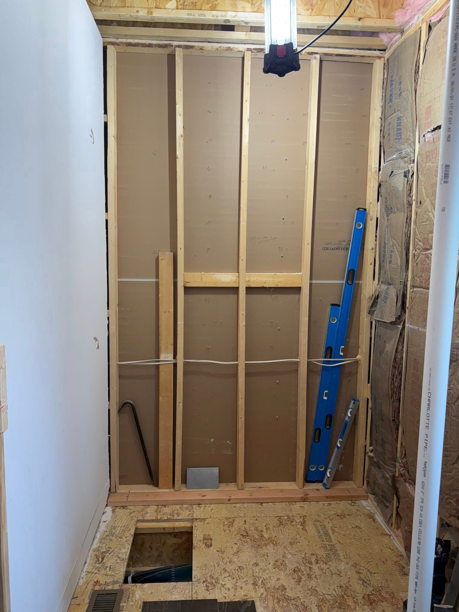 Partially renovated bathroom with exposed studs, insulation, and a blue ladder leaning against the wall