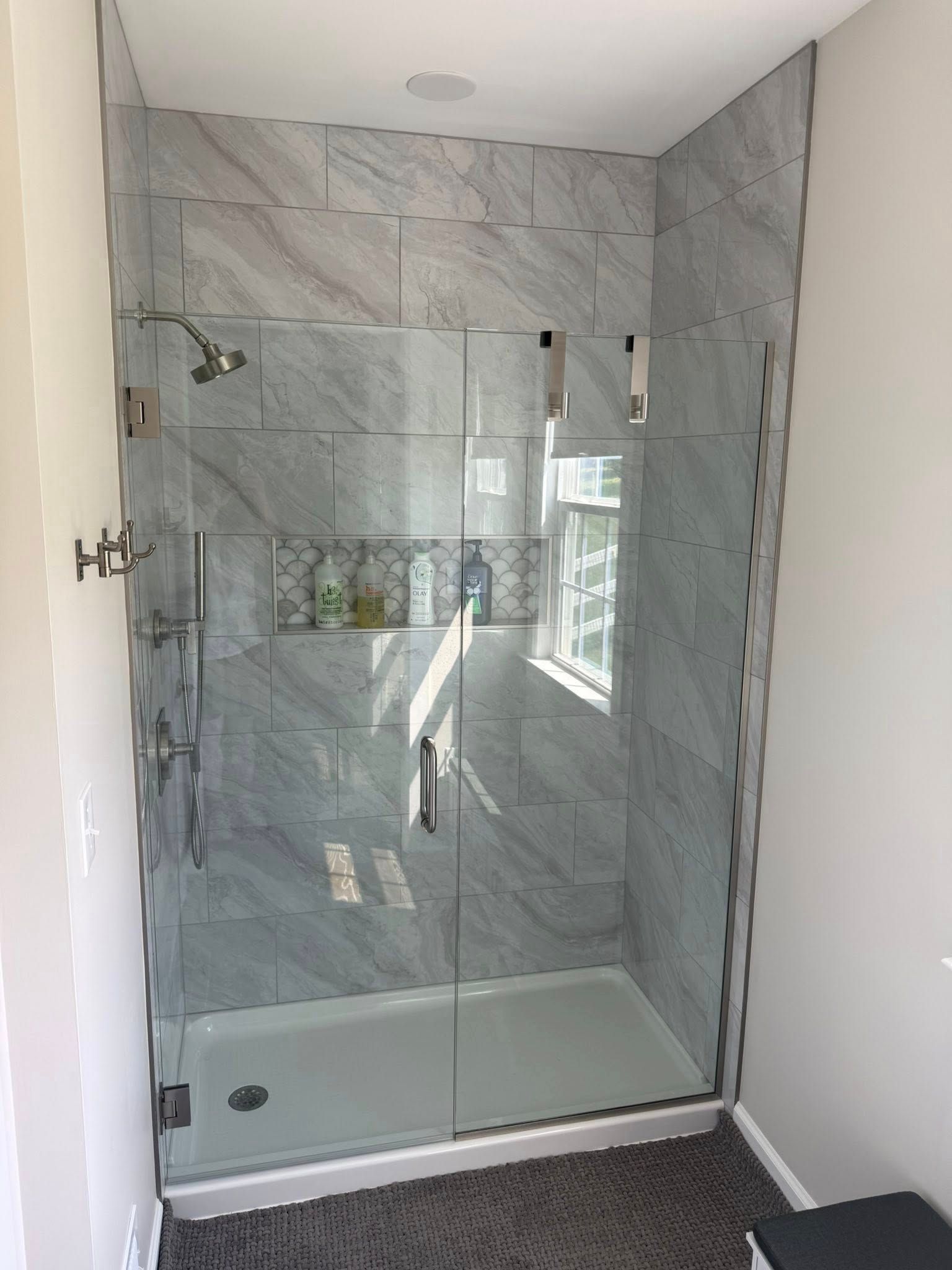 Modern glass shower with marble tile walls and white base in a bathroom