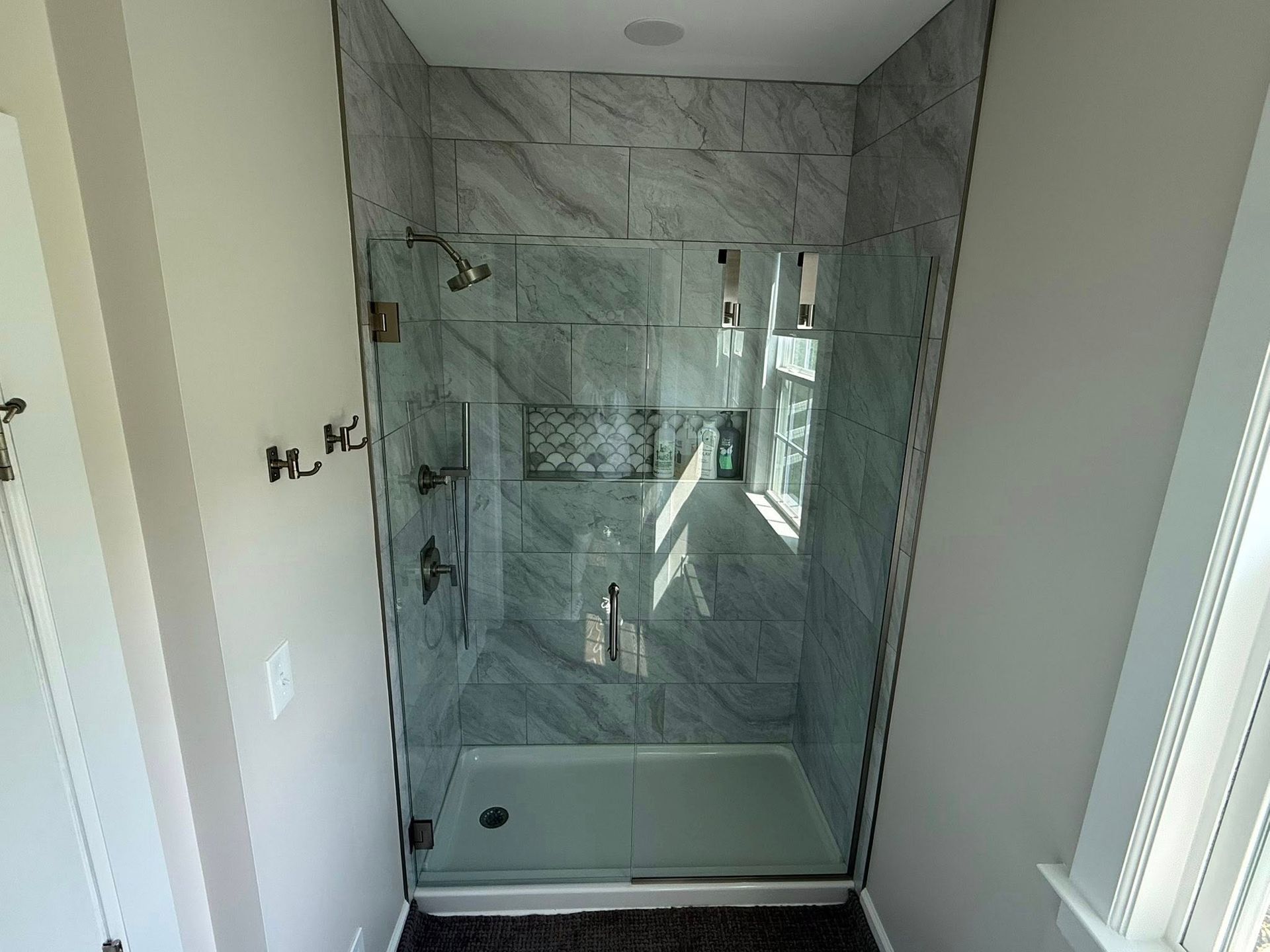 Marble-tiled bathroom shower with glass door and built-in bench.