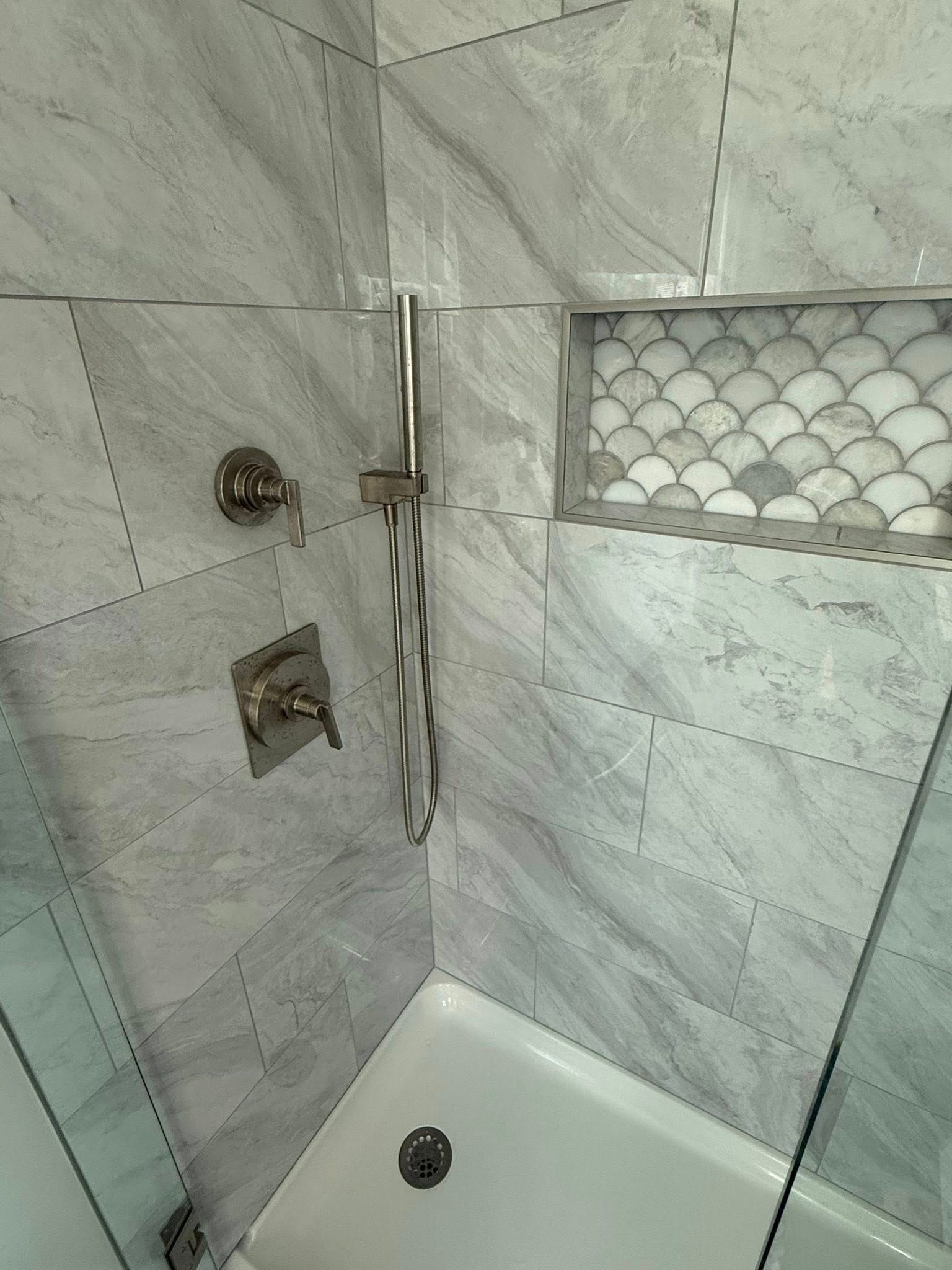 Tiled shower stall with chrome fixtures and a small hexagon-tile accent shelf.