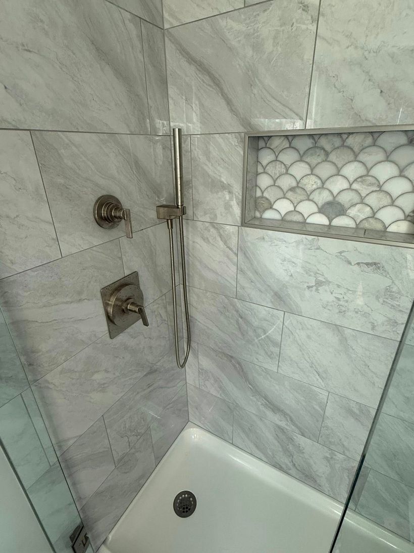 White-tiled shower stall with a chrome showerhead, controls, and a small glass-block window.