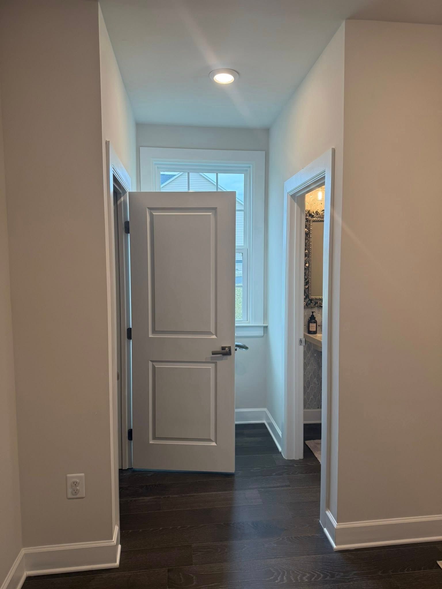 Narrow hallway with dark wood floor, open doorways, and a window at the end.