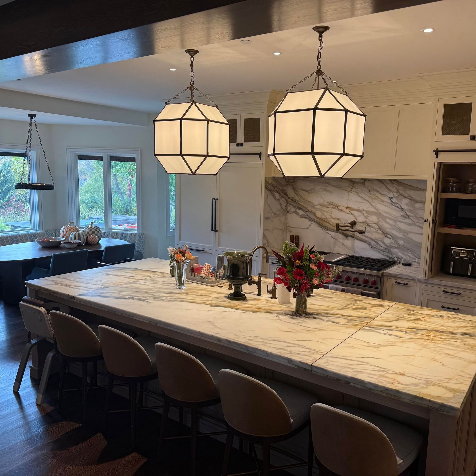 Modern kitchen with a large marble island, two pendant lights, bar stools, and a marble backsplash