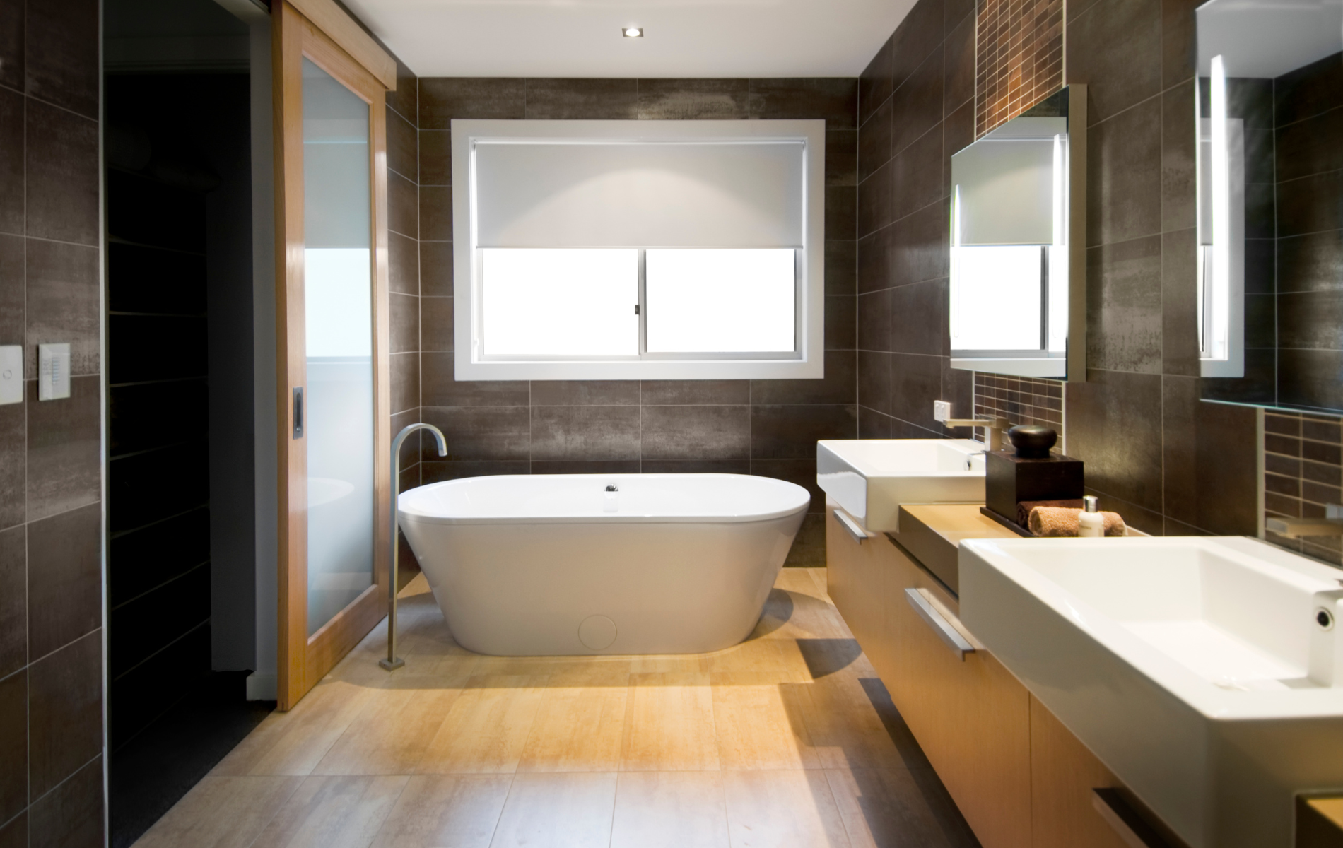 Modern bathroom with freestanding tub, double sink vanity, large mirror, and wood flooring.