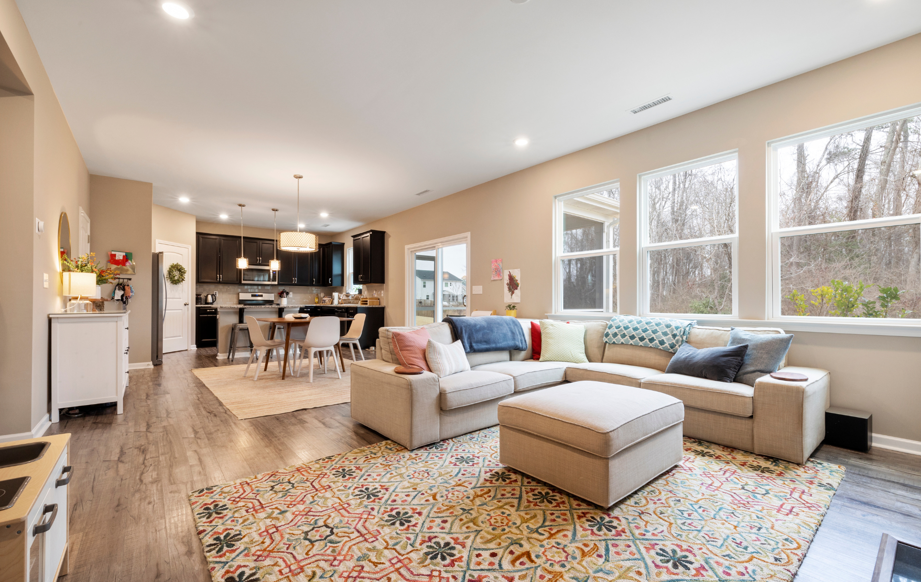 Bright open-plan living room with sectional sofa, colorful rug, and kitchen in the background