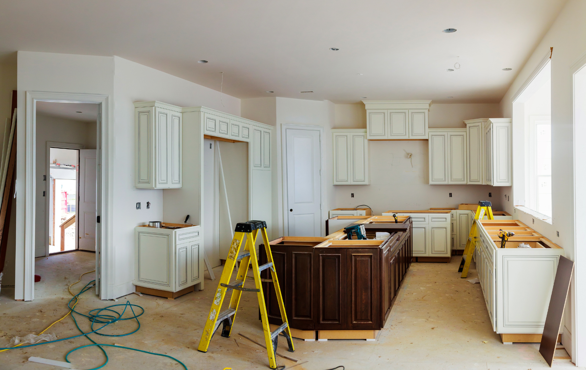 Kitchen under renovation with white cabinets, a yellow ladder, and tools on the floor