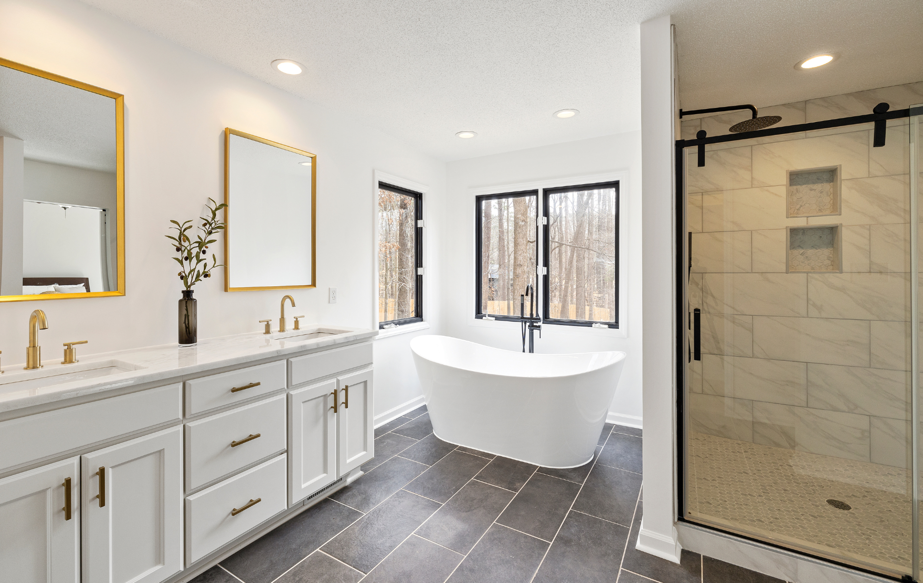 Modern bathroom with double vanity, freestanding tub, large windows, and glass-enclosed shower