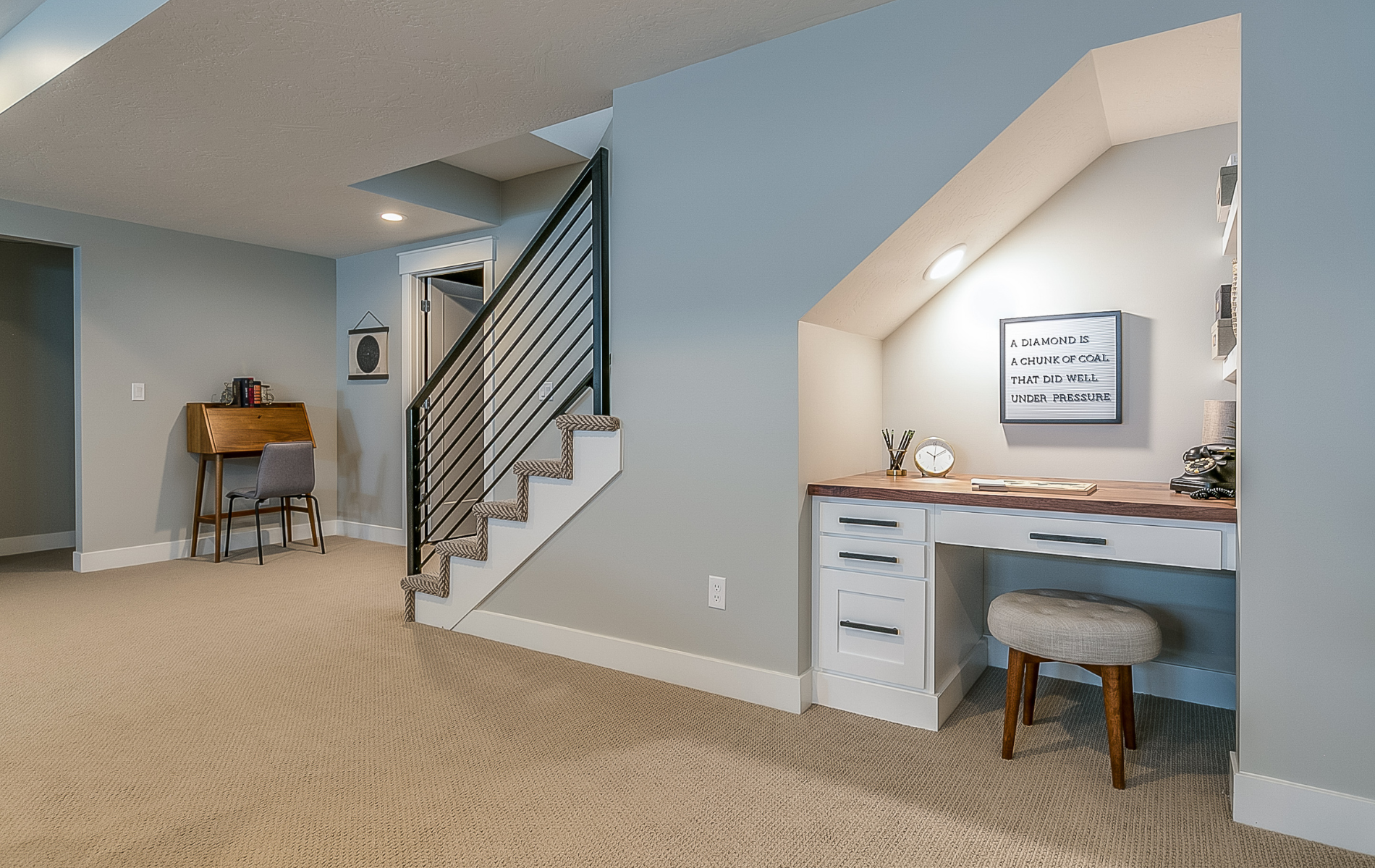 Carpeted living room with staircase and built-in desk nook under a sloped ceiling