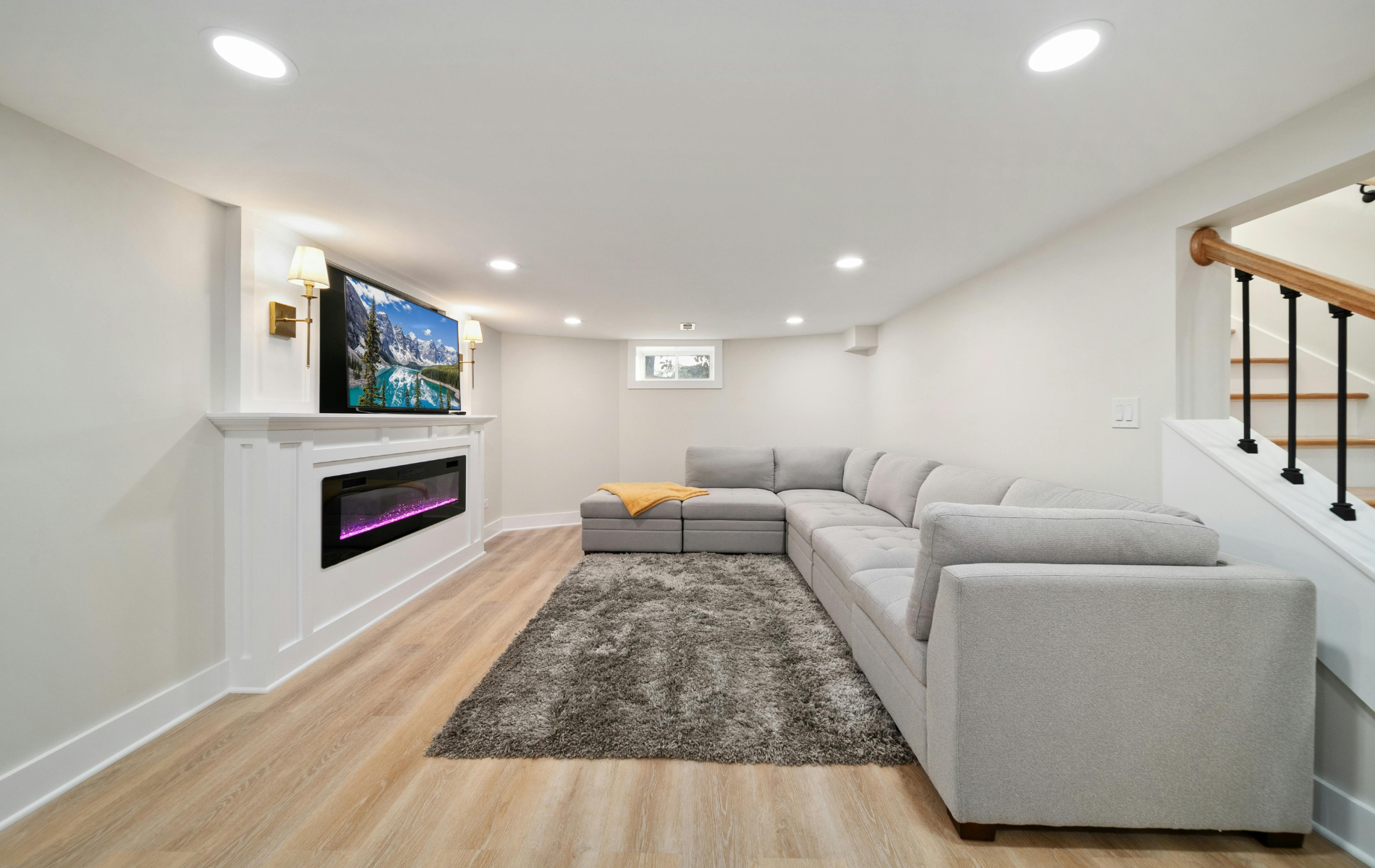 Modern living room with gray sectional, wall-mounted TV, electric fireplace, and light wood floors