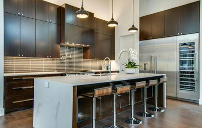 Modern kitchen with dark cabinets, marble island, bar stools, and stainless steel refrigerator