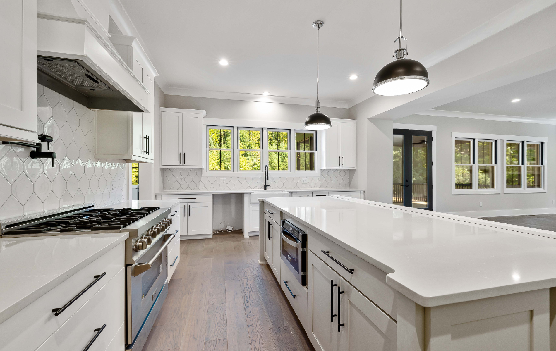 Bright modern kitchen with white cabinets, large island, stainless stove, and pendant lights