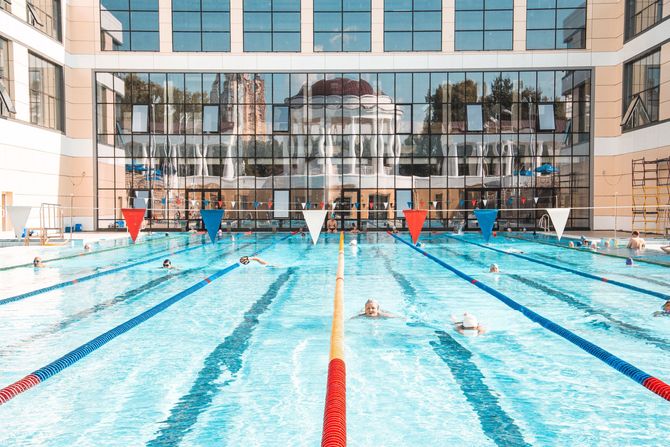 Indoor outdoor swimming pool with lane markers and people swimming in clear blue water
