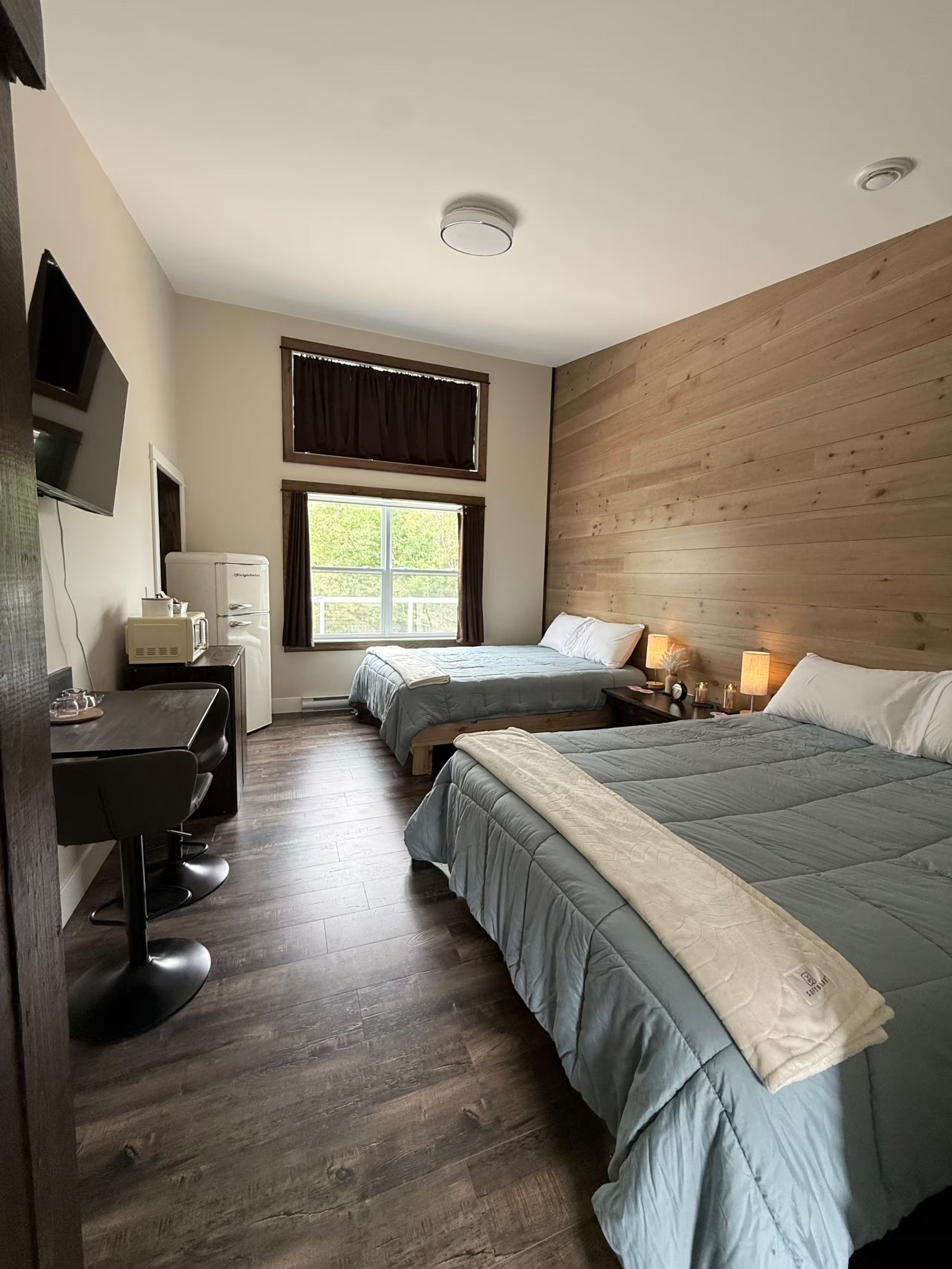 Hotel room with two twin beds, wood accent wall, TV, desk, and window with dark curtains