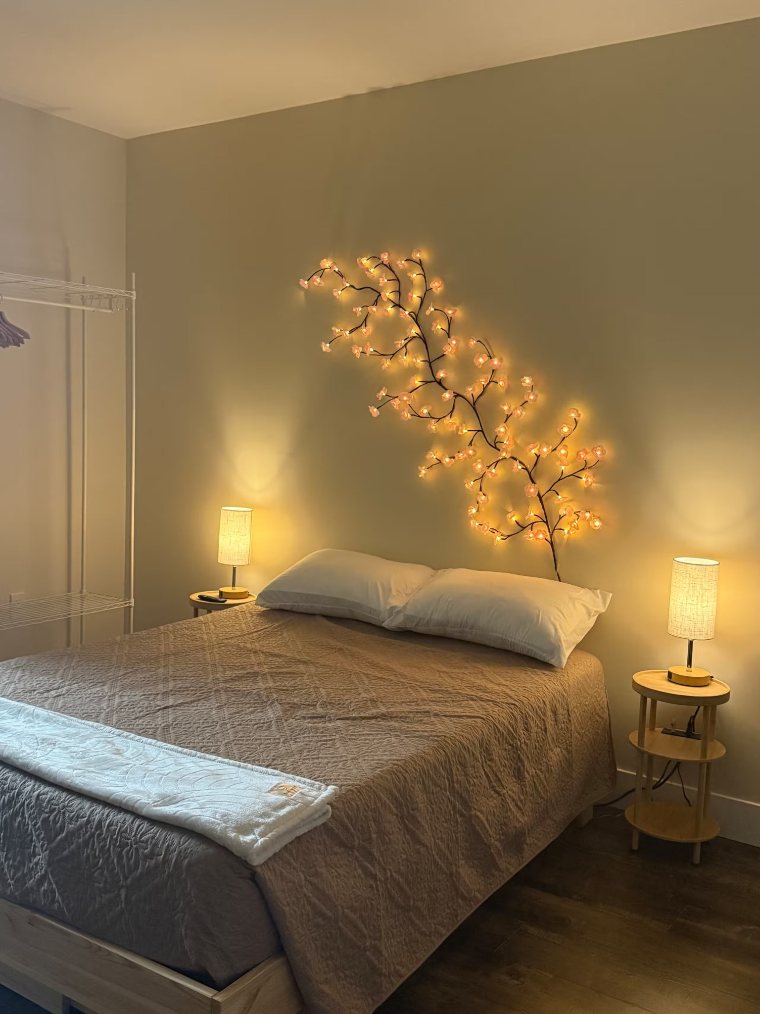 Cozy bedroom with gray bedspread, warm lamps, and glowing branch lights on a beige wall