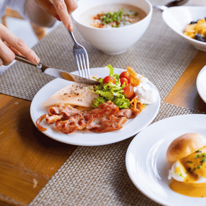 Dining table with plated meal and salad, a hand cutting meat with a fork and knife, and soup and bread nearby