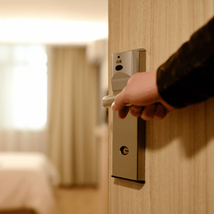 Hand opening a hotel room door with a card lock, blurred bed in the background