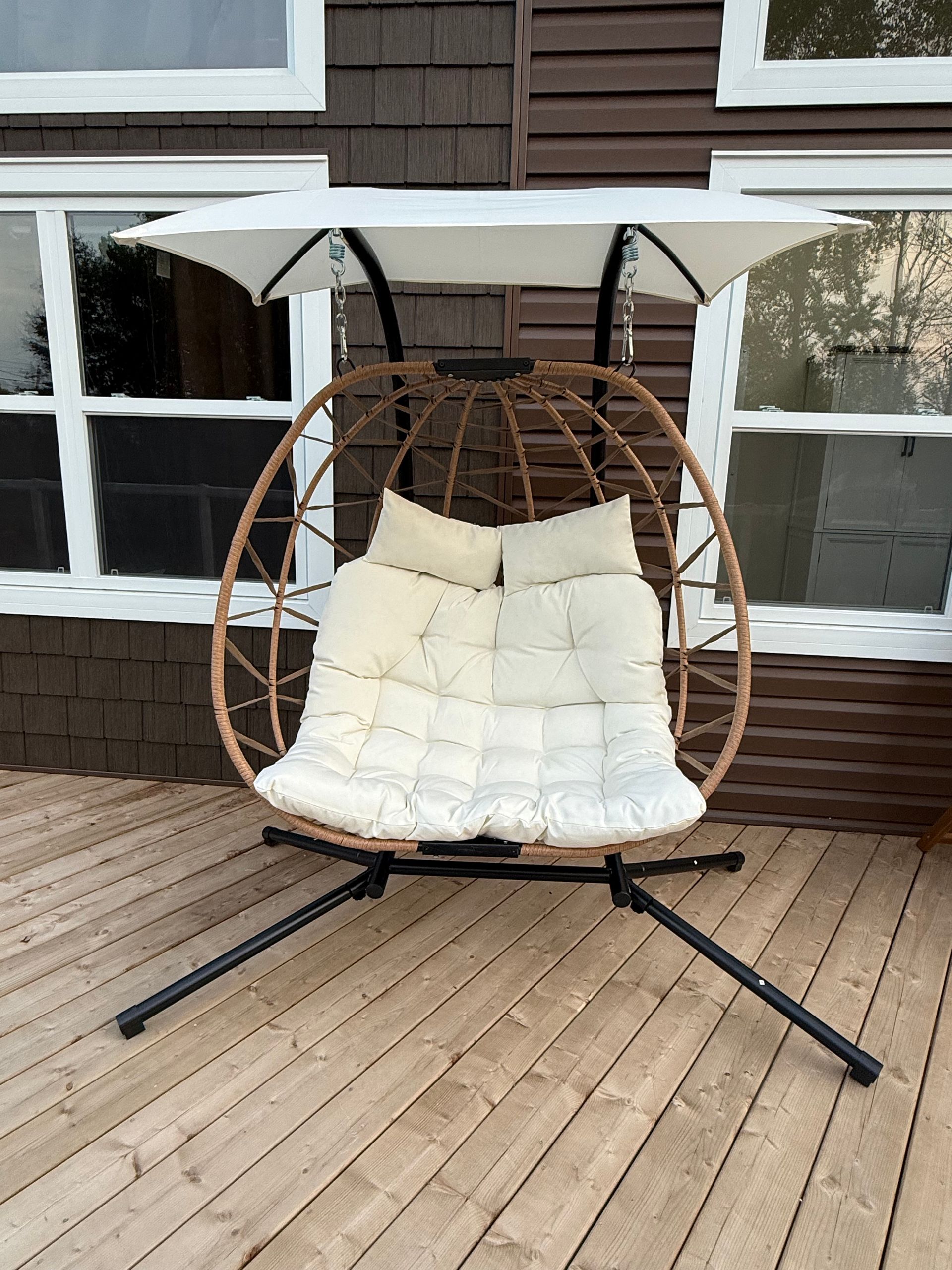 White hanging egg chair with cushion on a wooden deck in front of a house window