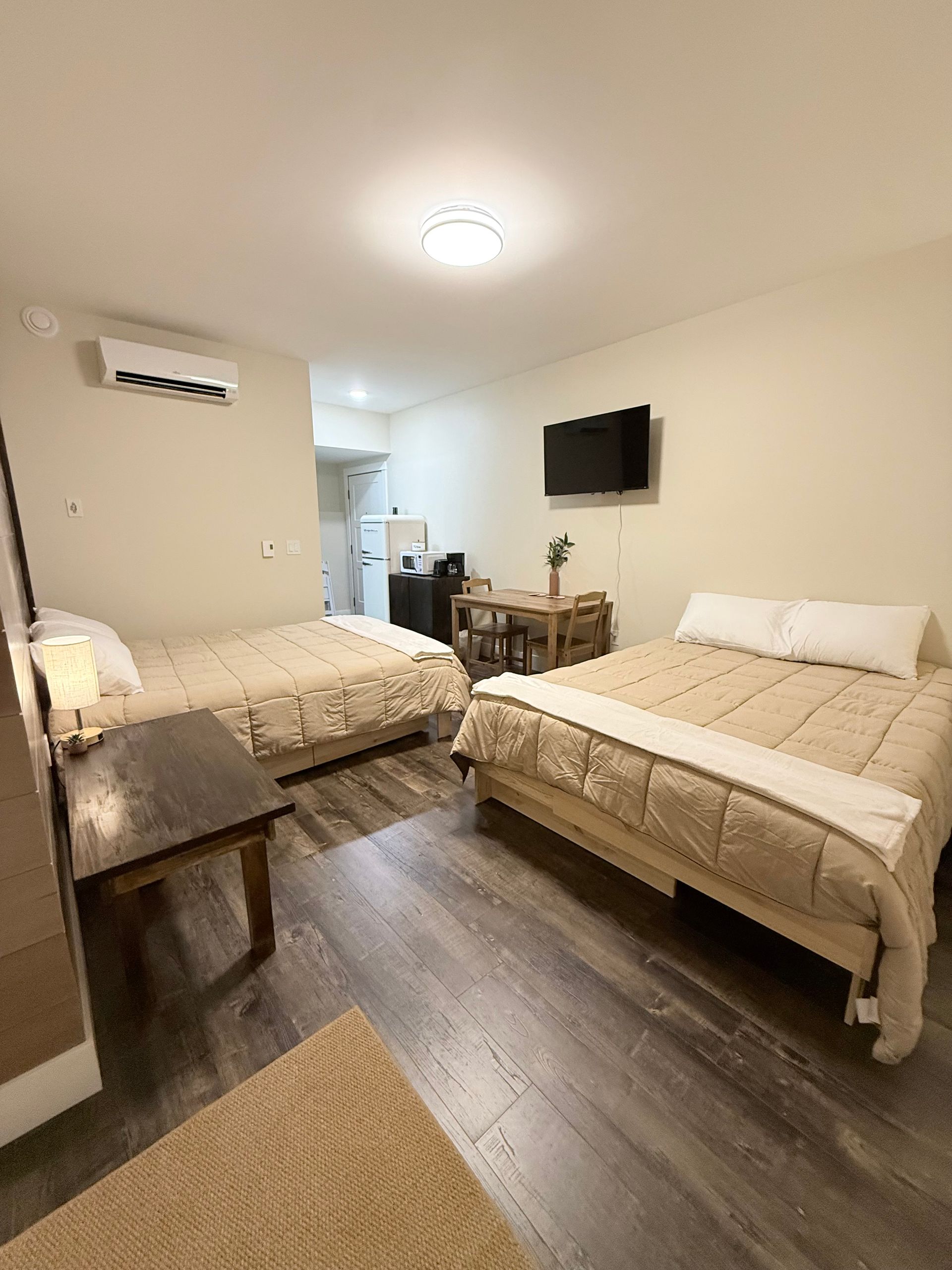 Small bedroom with two beds, wall-mounted TV, desk, and warm wood flooring.