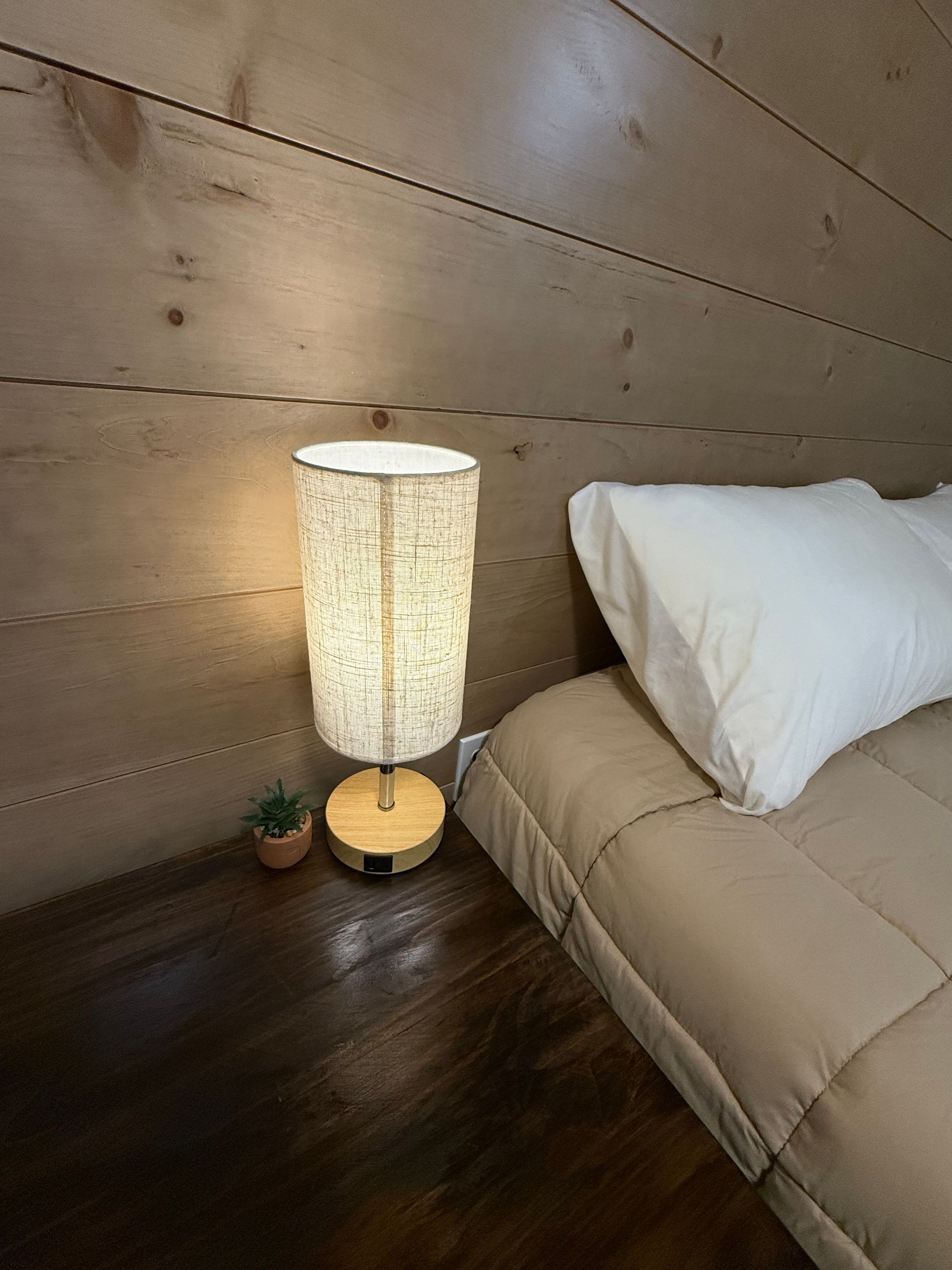 Cozy bedroom corner with bed, glowing floor lamp, small plant, and wood-paneled wall